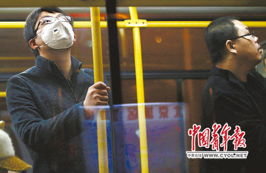 北京某公交车内，一位男青年戴着口罩抬头张望。